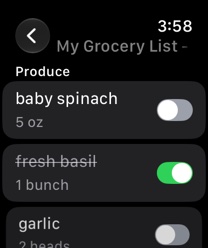A grocery list open on Apple Watch: baby spinach, fresh basil crossed off as purchased, and garlic, each with a switch.